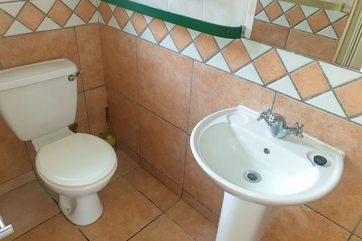 A compact bathroom featuring a pedestal basin and toilet with dated terracotta-style wall and floor tiling.