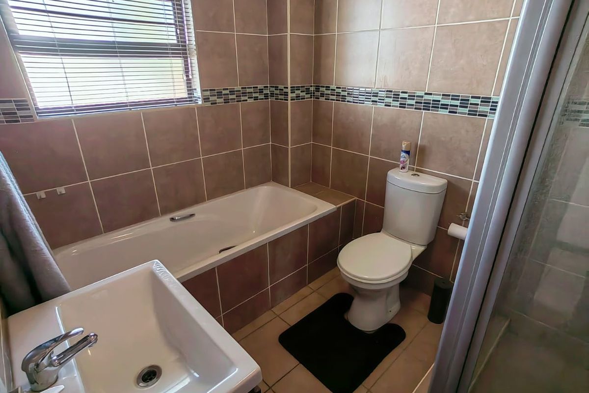 A functional bathroom featuring a built-in bathtub, a standard toilet, and a vanity basin with tiled walls and flooring.