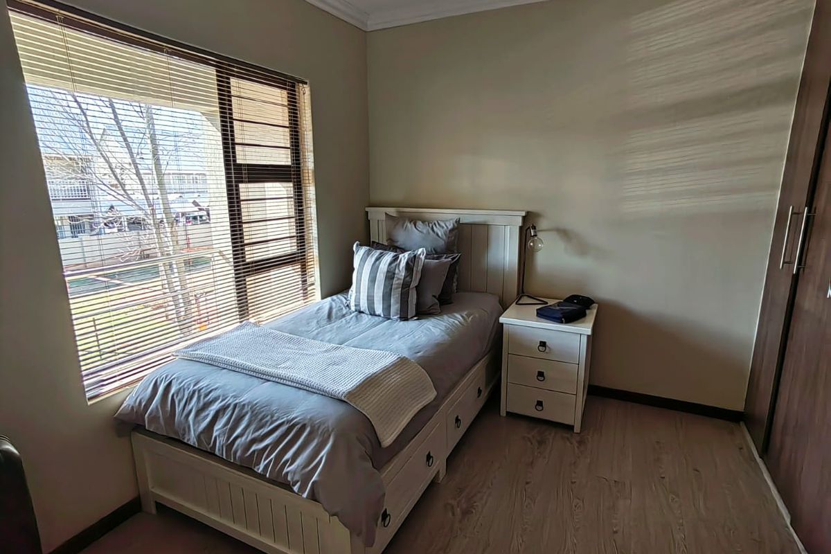 A well-lit bedroom featuring light wood-look flooring, neutral wall tones, and a large window with fitted blinds, providing a comfortable and functional living space.