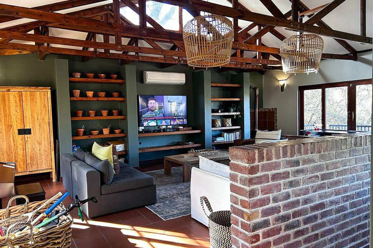 Spacious living area featuring exposed timber roof trusses, terracotta tiled flooring, built-in shelving, and a feature face-brick partition wall.