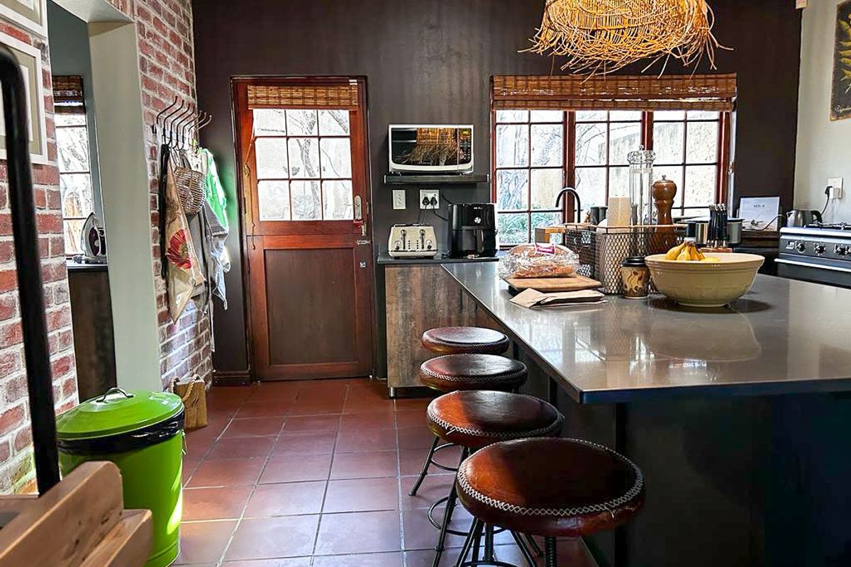 A rustic-style kitchen featuring a central island with stone countertop, exposed brick wall accents, tiled flooring, and direct access to the exterior.