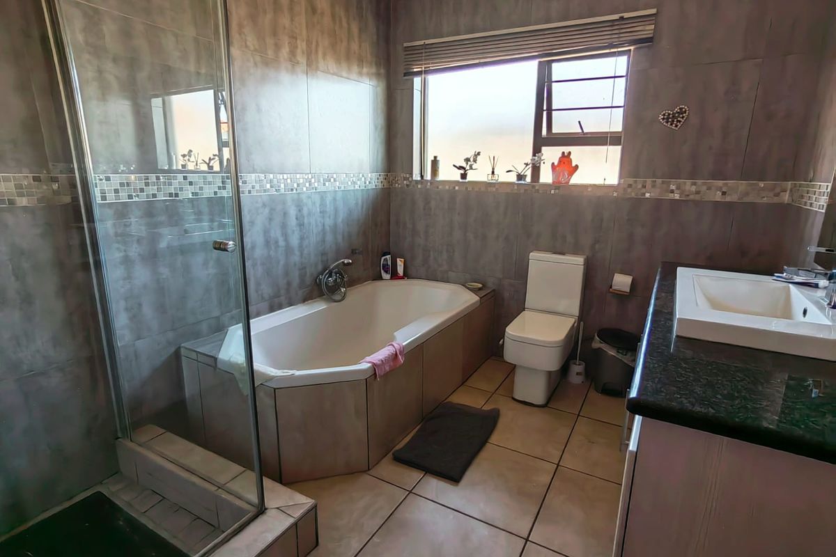 A functional bathroom featuring a built-in bathtub, glass-enclosed shower, modern toilet, and a vanity with a stone countertop.