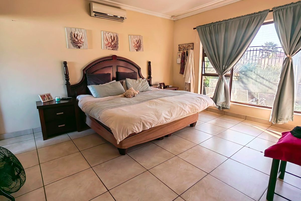Spacious bedroom featuring large ceramic floor tiles, a wall-mounted air conditioning unit, and a large window providing natural light.