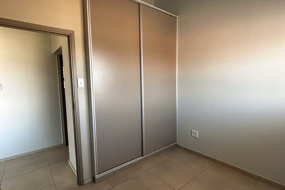 A clean bedroom featuring neutral floor tiles and built-in sliding door cupboards, offering a functional and well-maintained storage solution.