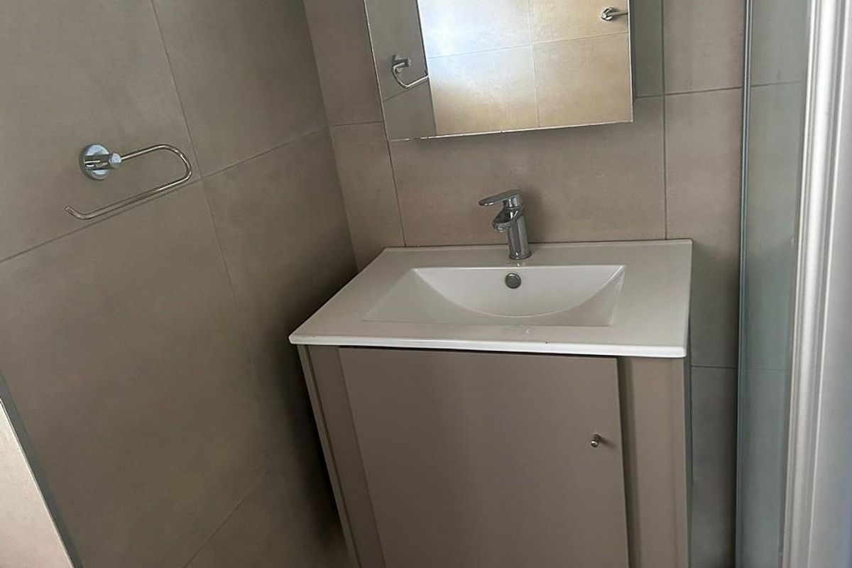 A compact bathroom featuring a modern vanity with a white basin, chrome faucet, and a wall-mounted mirror, complemented by neutral wall tiling.