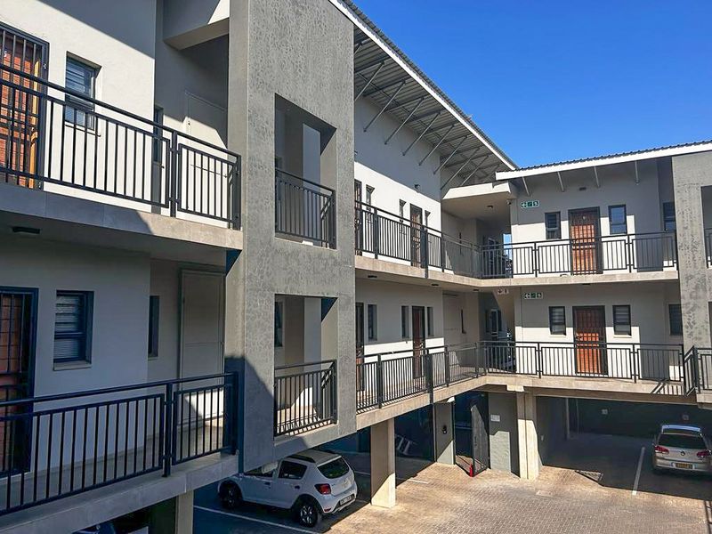 Exterior view of a modern apartment complex featuring multi-level walkways, metal railings, and covered ground-level parking.