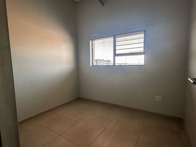 A clean, empty bedroom featuring neutral tiled flooring and a window with fitted blinds, offering a versatile space ready for personalization.