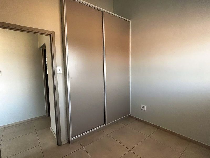 A clean bedroom featuring neutral floor tiles and built-in sliding door cupboards, offering a functional and well-maintained storage solution.