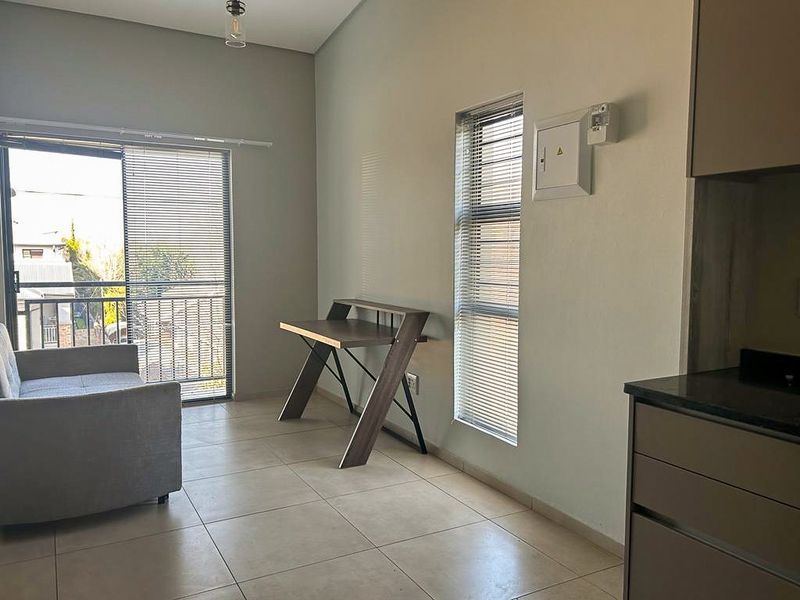 Open plan living area featuring tiled flooring, large sliding doors leading to a balcony, and a modern kitchen corner with built-in cabinetry.