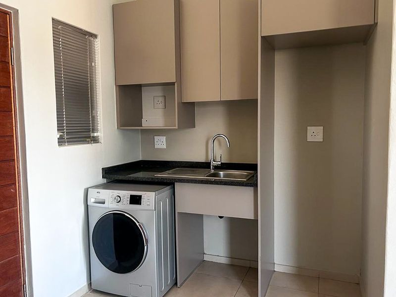 A functional laundry area featuring built-in cabinetry, a stainless steel sink, and dedicated space for a washing machine and additional appliance.