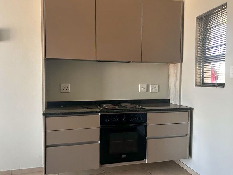 Modern kitchen featuring sleek cabinetry, a built-in oven, electric hob, and dark stone countertops, providing a clean and functional cooking space.