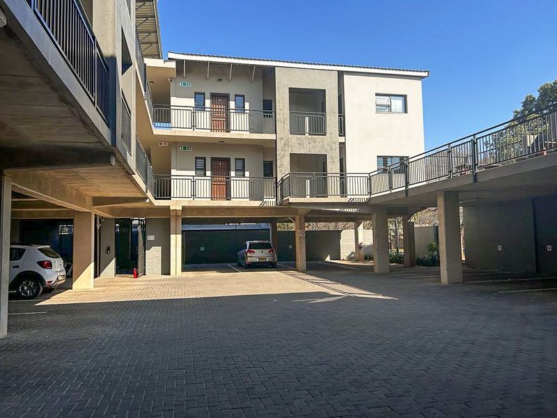 Exterior view of a modern apartment complex featuring covered parking bays, concrete pillars, and metal balcony railings.
