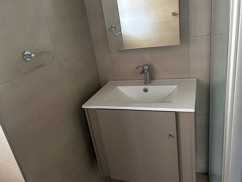 A compact bathroom featuring a modern vanity with a white basin, chrome faucet, and a wall-mounted mirror, complemented by neutral wall tiling.