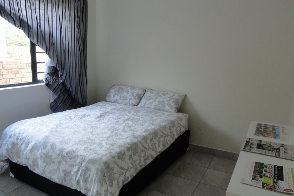 A standard bedroom featuring tiled flooring and a window with security bars, providing a functional and neutral living space.