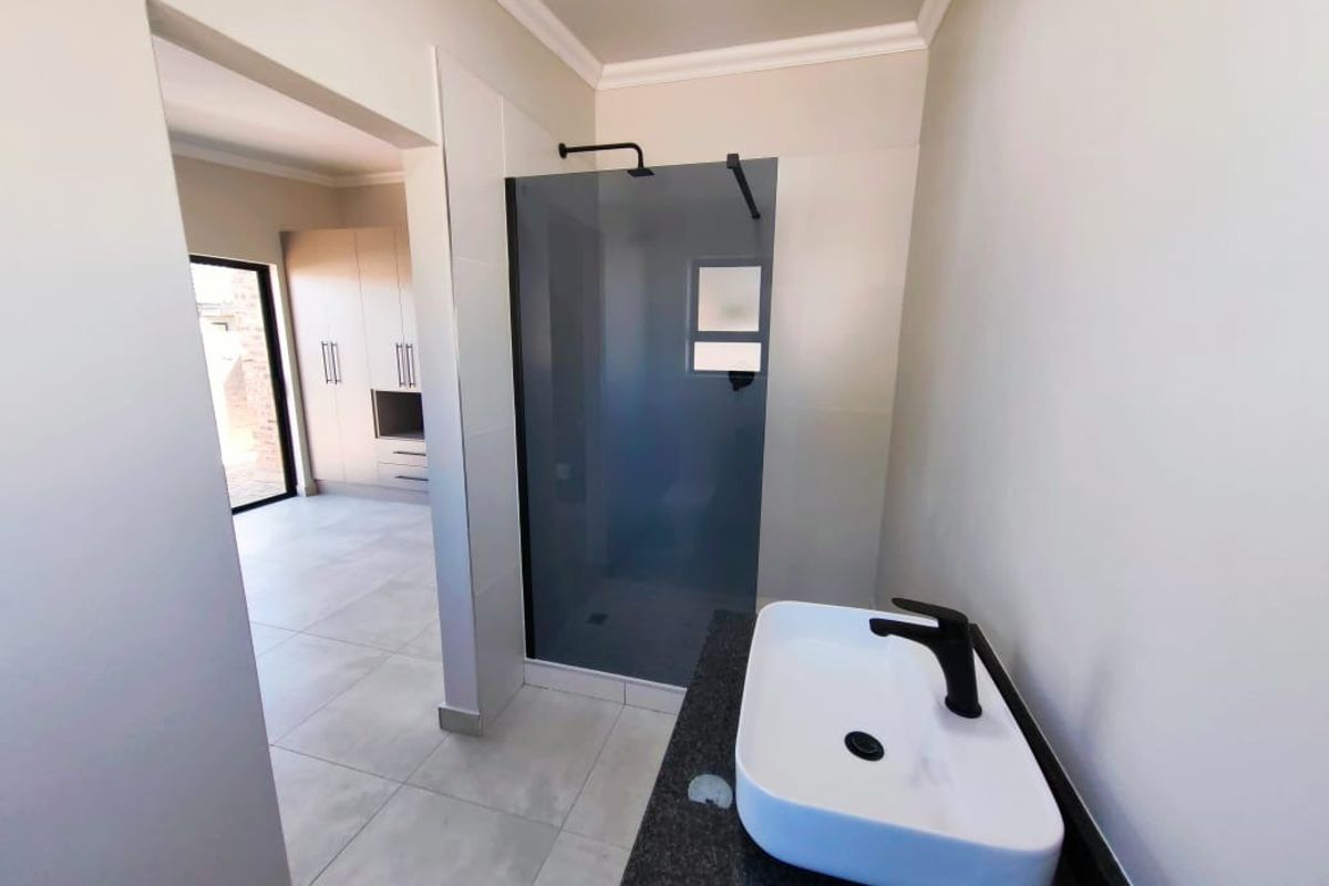 Modern bathroom featuring a walk-in shower with dark glass screen, black fixtures, and a contemporary vessel sink on a stone vanity top.