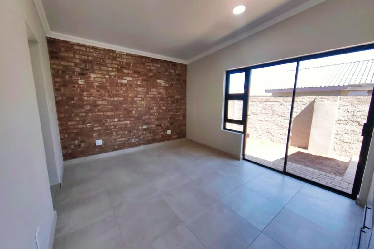 A bright, empty bedroom featuring a modern exposed brick feature wall, large format floor tiles, and sliding glass doors leading to an outdoor area.