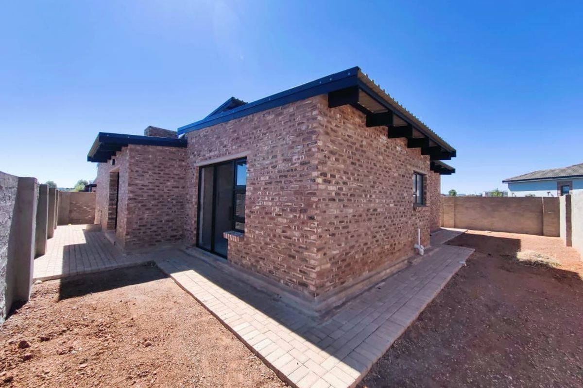 Rear view of a modern face-brick house featuring a paved walkway, sliding glass doors, and exposed roof rafters.