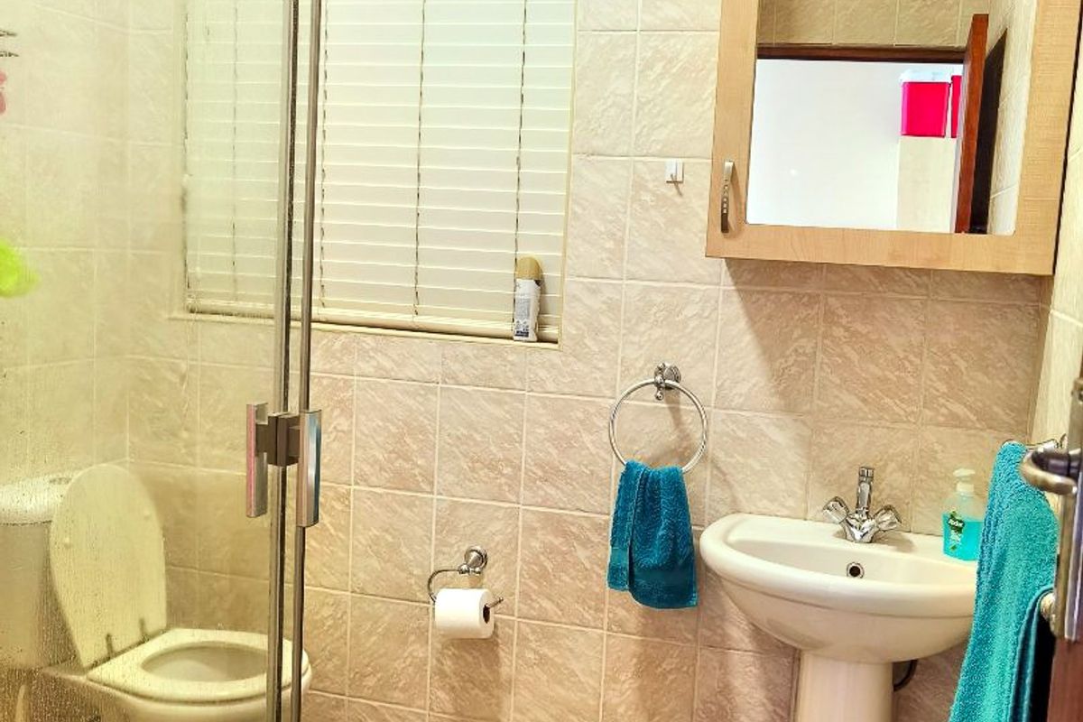 A functional bathroom featuring a glass-enclosed shower, pedestal basin, wall-mounted mirror cabinet, and neutral floor-to-ceiling wall tiling.