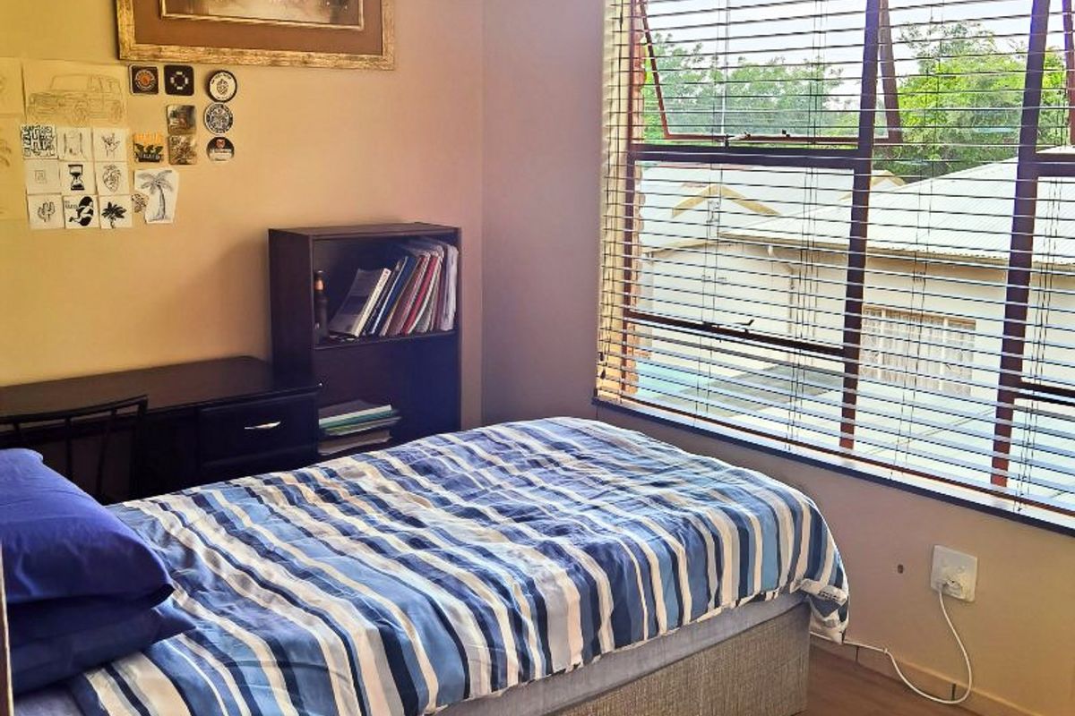 A functional bedroom featuring wood-look flooring, large window with fitted blinds, and neutral wall finishes.
