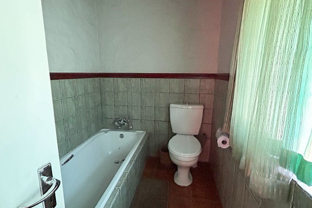 A functional bathroom featuring a standard bathtub, toilet, and partial wall tiling, requiring cosmetic updates to modernize the space.