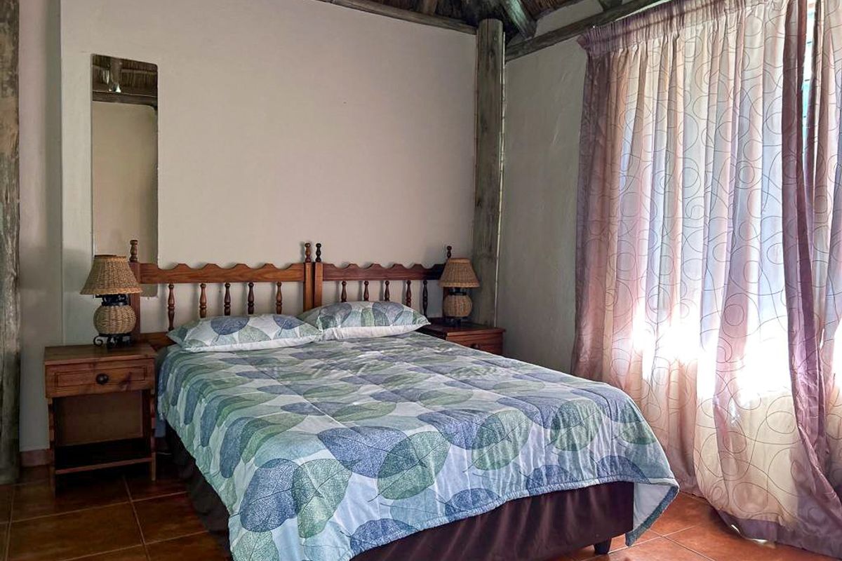 A rustic bedroom featuring a thatched roof ceiling, tiled flooring, and large windows with curtains, creating a cozy and traditional atmosphere.
