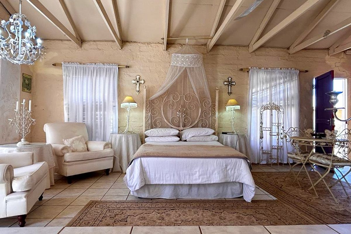 Spacious bedroom featuring exposed timber ceiling beams, tiled flooring, and rustic textured walls, creating a warm and character-filled living space.