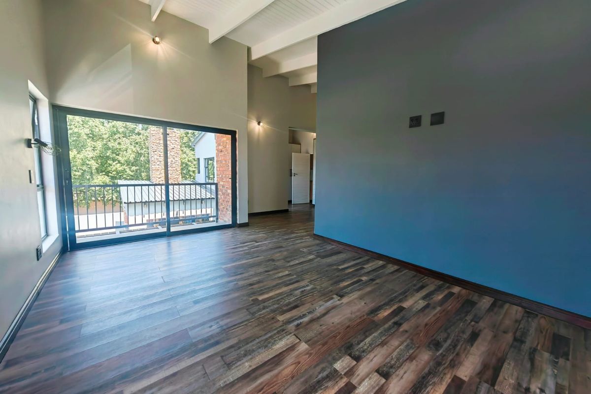 Spacious living area featuring high vaulted ceilings with exposed beams, dark wood-look flooring, and large sliding glass doors opening to a balcony.