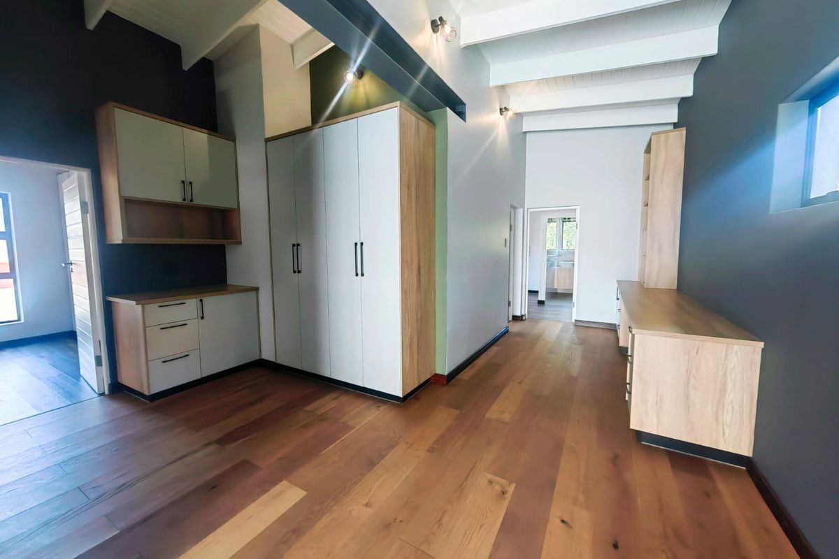 A modern, spacious room featuring high vaulted ceilings with exposed beams, built-in cabinetry, and warm timber flooring.