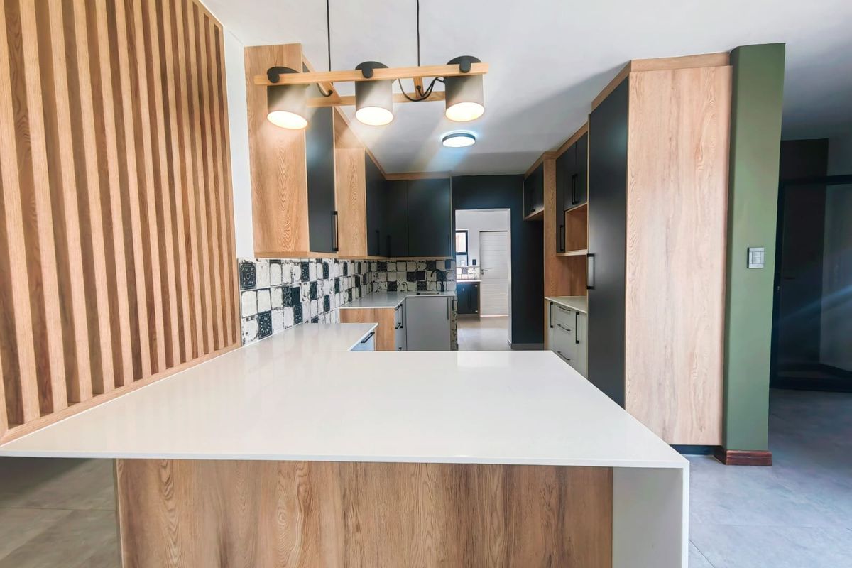 Modern kitchen featuring wood-grain cabinetry, contrasting dark matte cupboards, white stone countertops, and a decorative timber slat feature wall.