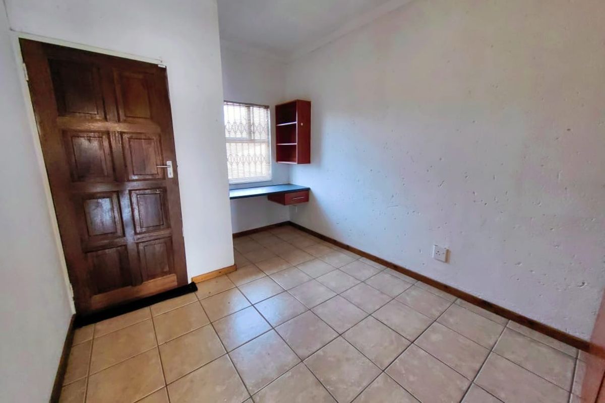 A functional bedroom or study space featuring tiled flooring, a built-in desk with shelving, and a solid timber door.