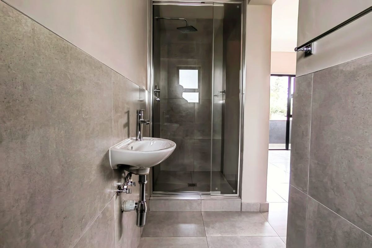 Modern bathroom featuring a glass-enclosed shower with a rainfall showerhead and a wall-mounted basin with chrome fixtures.