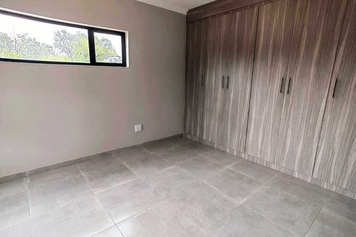 A clean, modern bedroom featuring large-format floor tiles, neutral wall tones, and extensive built-in wooden cabinetry.