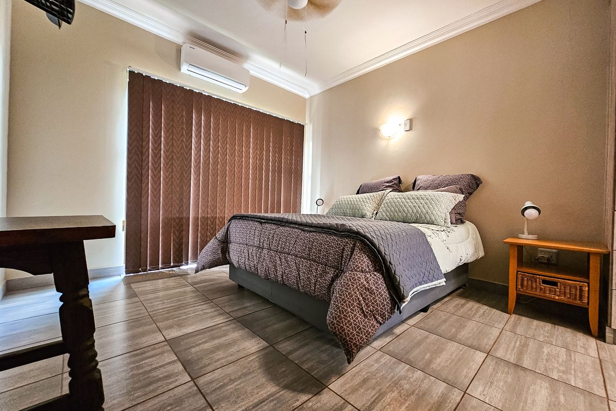 A bedroom featuring tiled flooring, a wall-mounted air conditioning unit, vertical blinds, and crown molding.