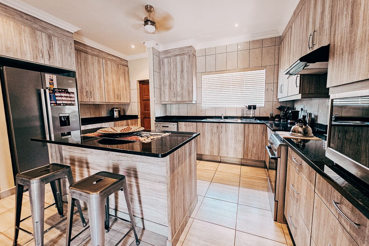Modern kitchen featuring wood-grain cabinetry, black granite countertops, a central island with breakfast bar, and integrated stainless steel appliances.
