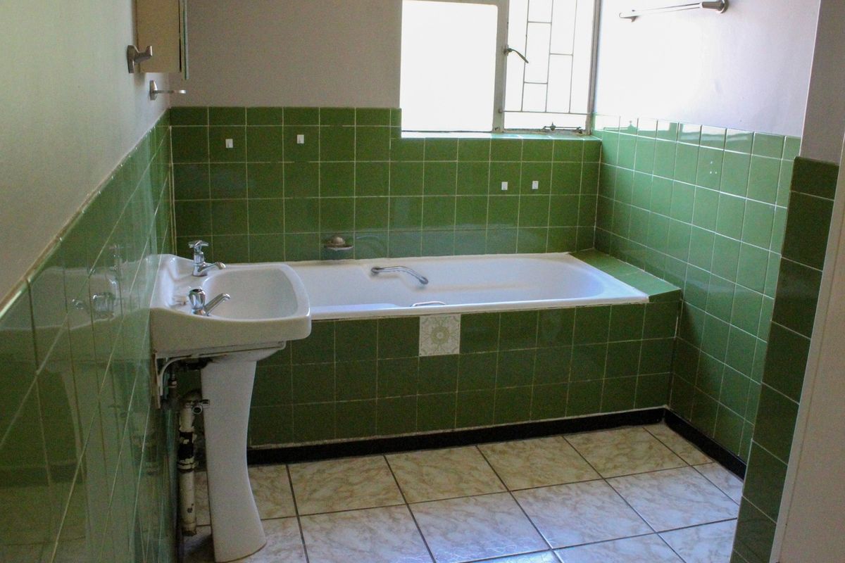 A dated bathroom featuring green wall tiles, a built-in bathtub, and a pedestal sink with exposed plumbing.