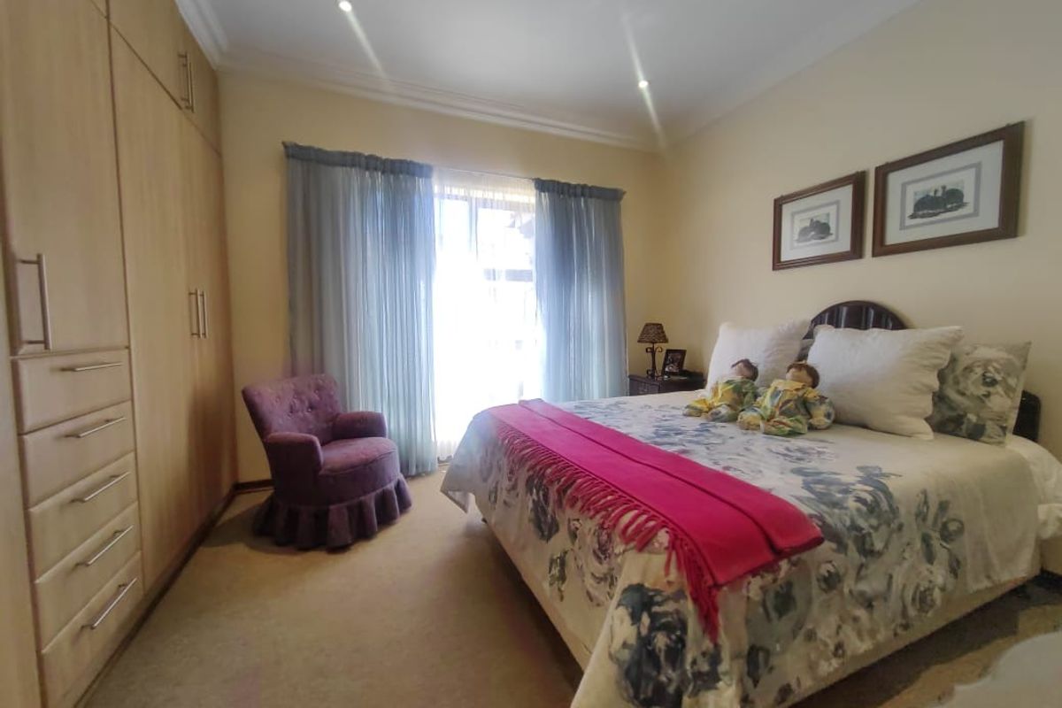 A well-maintained bedroom featuring extensive built-in wooden cabinetry, neutral carpeting, and large windows allowing for natural light.
