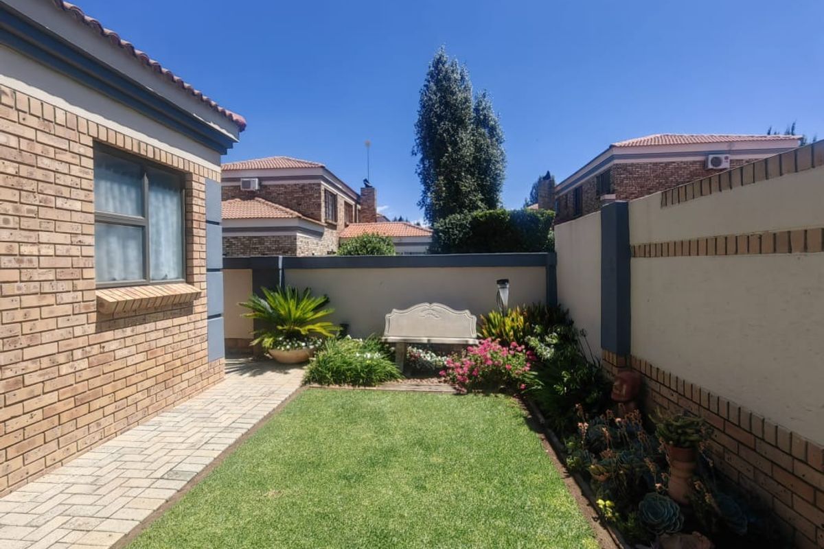 A private rear garden featuring a manicured lawn, paved walkway, and perimeter boundary walls, offering a peaceful outdoor space for the townhouse.