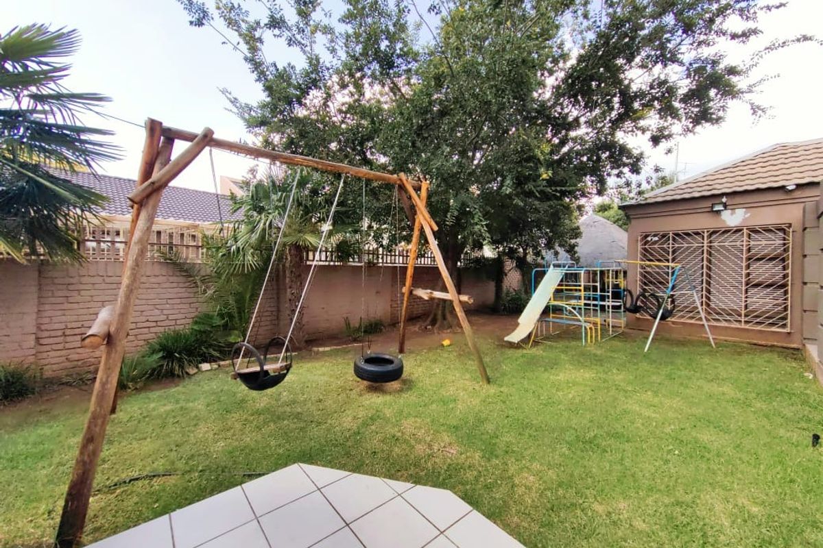 A private rear garden featuring a lawn area, established trees, and a paved patio section adjacent to the main house structure.
