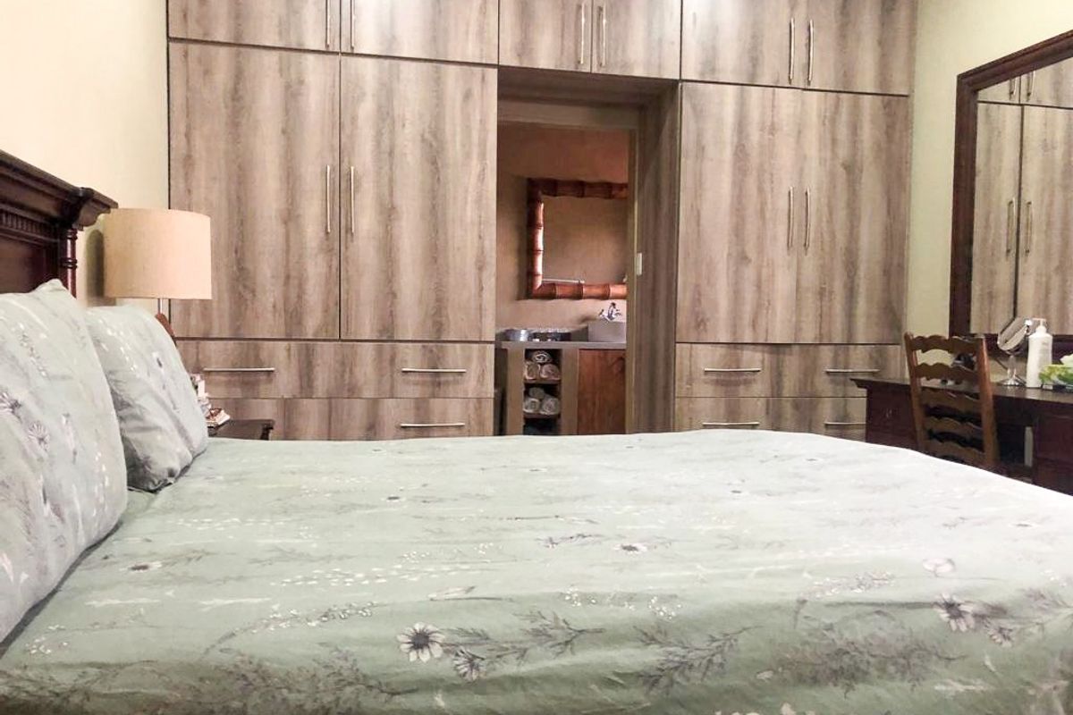 A well-maintained bedroom featuring extensive floor-to-ceiling built-in wooden cabinetry and an integrated vanity area, with an adjoining bathroom visible through the doorway.
