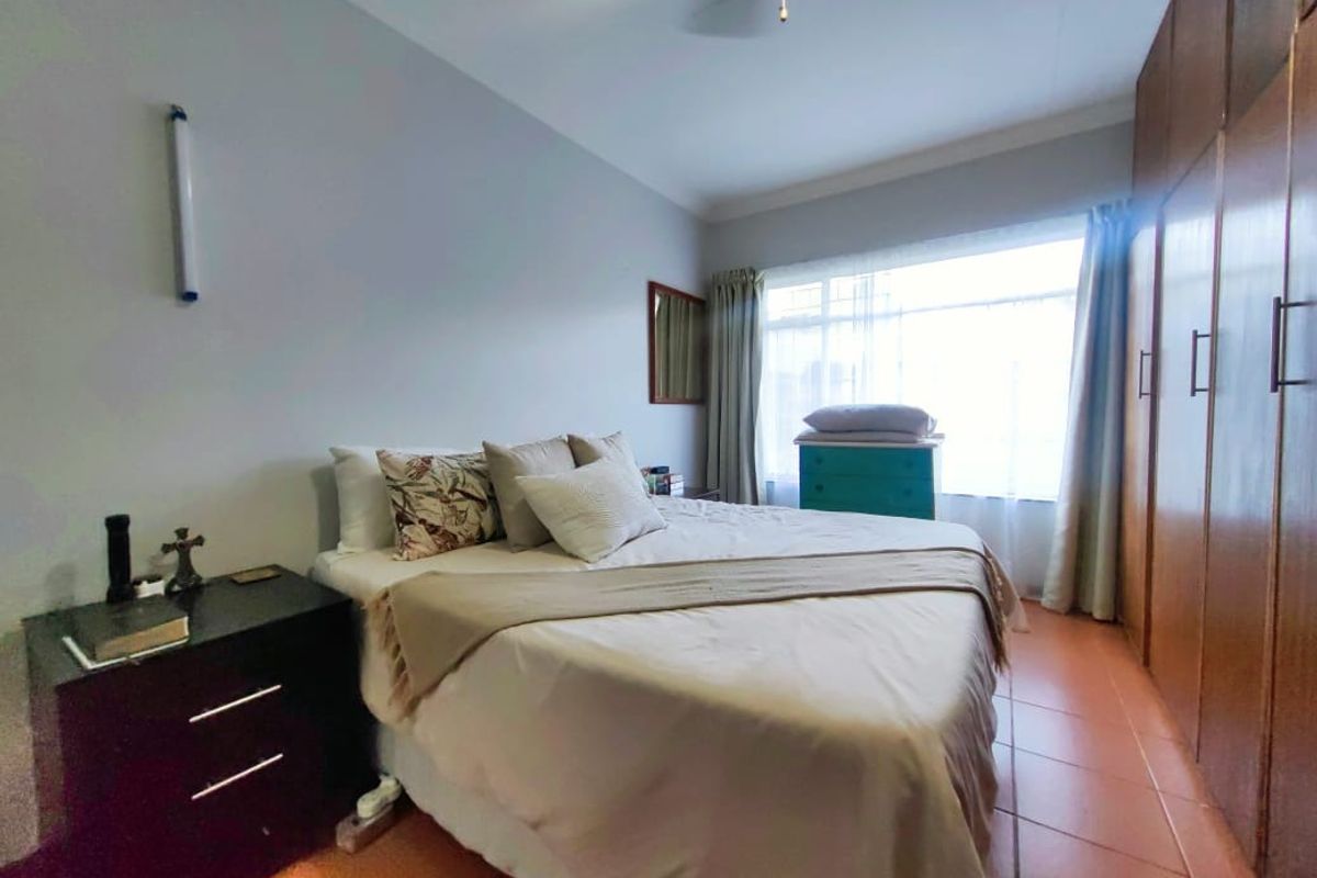 A bedroom featuring built-in wooden cupboards, tiled flooring, and a large window allowing natural light.