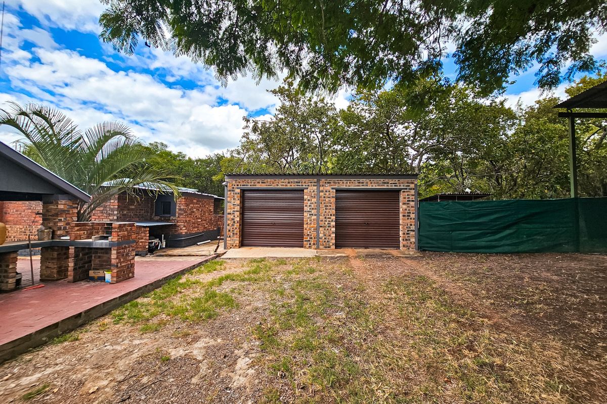 A double garage with brick facade and roller doors, featuring an adjacent outdoor brick-built braai area in a rural farm setting.