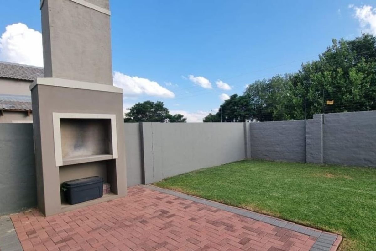 Private rear garden featuring a paved patio area with a built-in braai fireplace and a well-maintained lawn enclosed by perimeter walls.