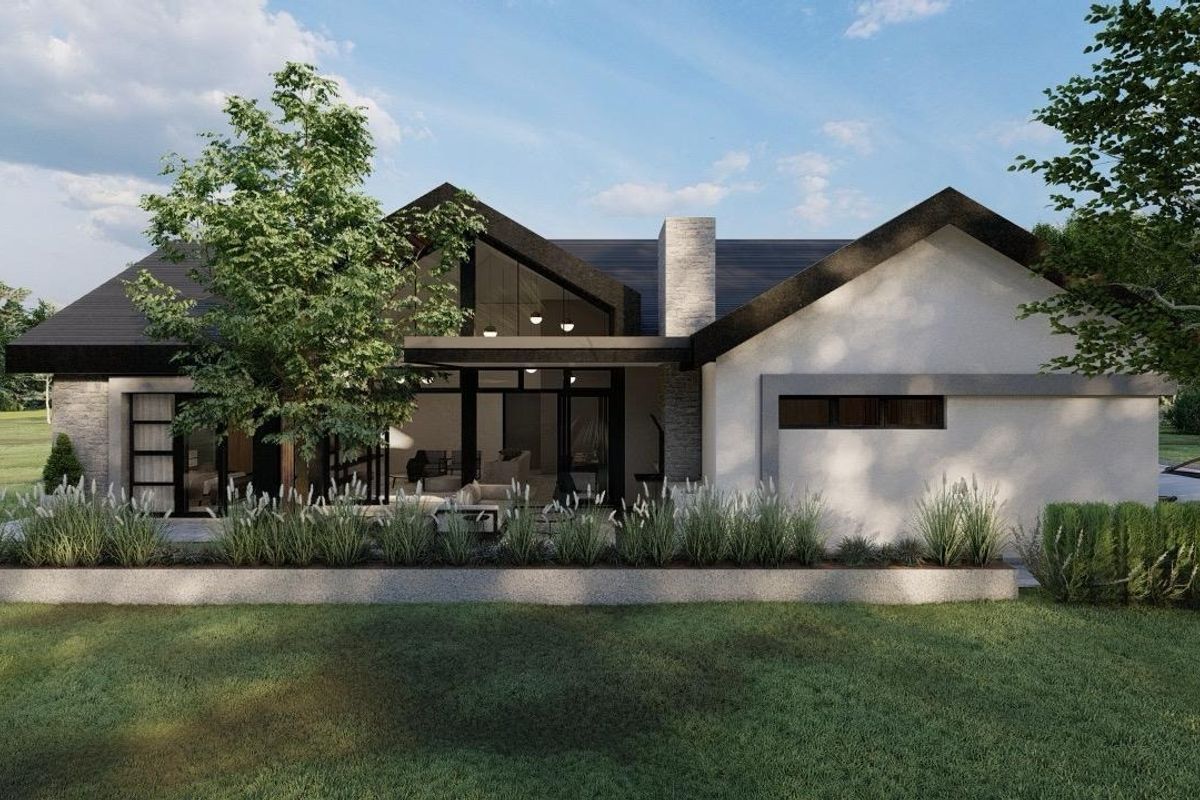 A modern architectural exterior view of a house featuring a pitched roof, stone chimney, and large glass windows overlooking a landscaped garden.