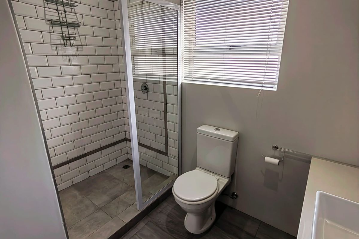 Modern bathroom featuring a walk-in shower with subway tile surround, a contemporary toilet, and a vanity basin.