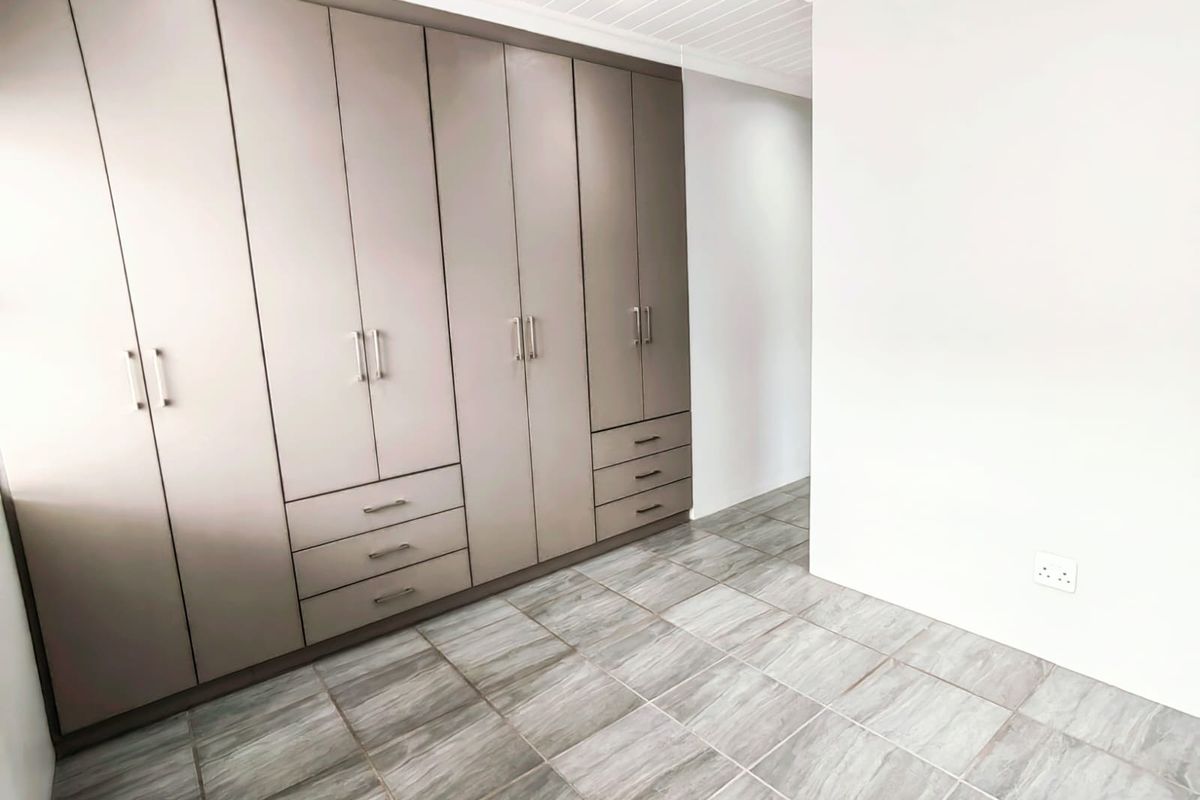 A bright bedroom featuring extensive built-in cabinetry with integrated drawers and modern tiled flooring.