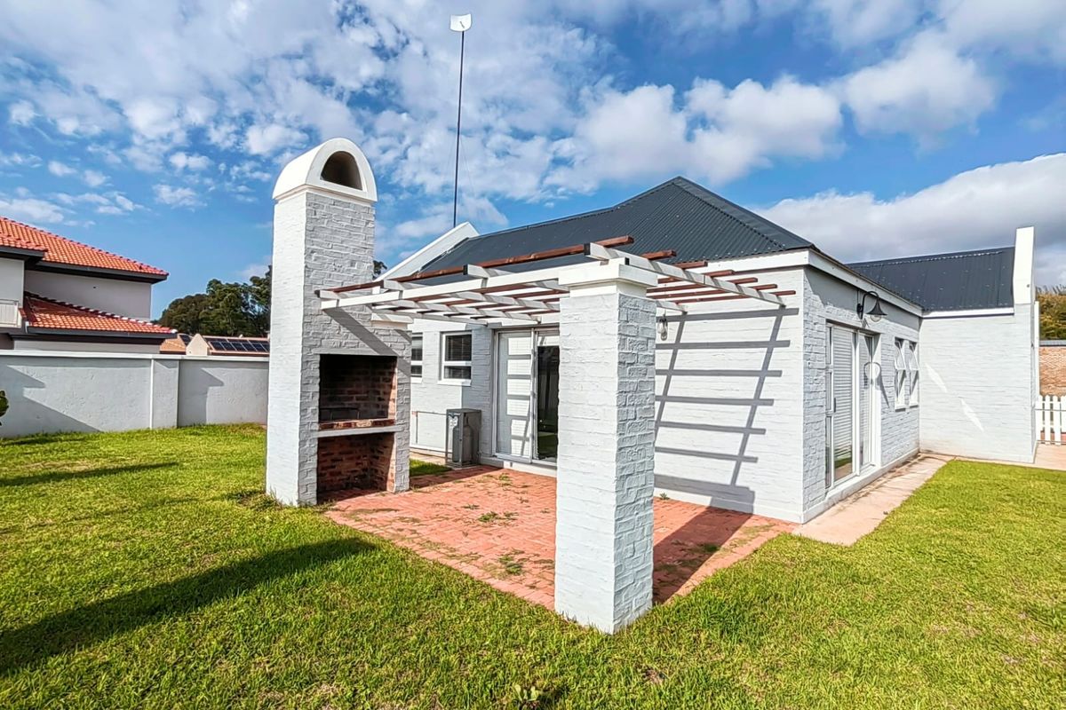 Rear exterior view featuring a paved patio area with a built-in brick braai, pergola structure, and access to the home via sliding glass doors.