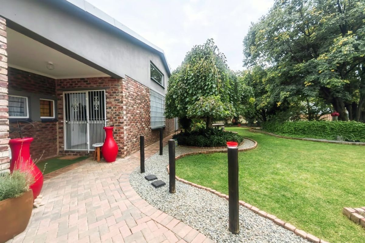 A well-maintained rear garden featuring a paved patio area, brick facade, manicured lawn, and established trees.