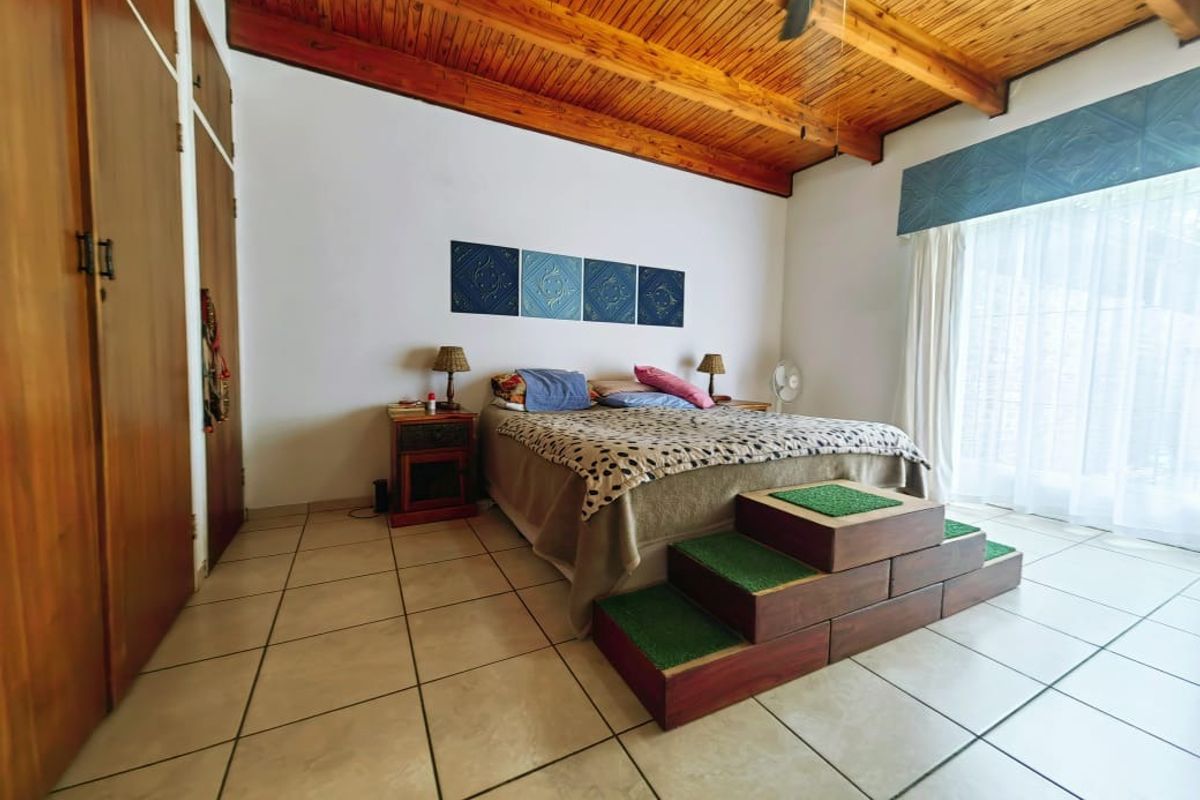 Spacious bedroom featuring a high exposed timber beam ceiling, tiled flooring, and built-in wooden cupboards with direct access to the outdoor area.