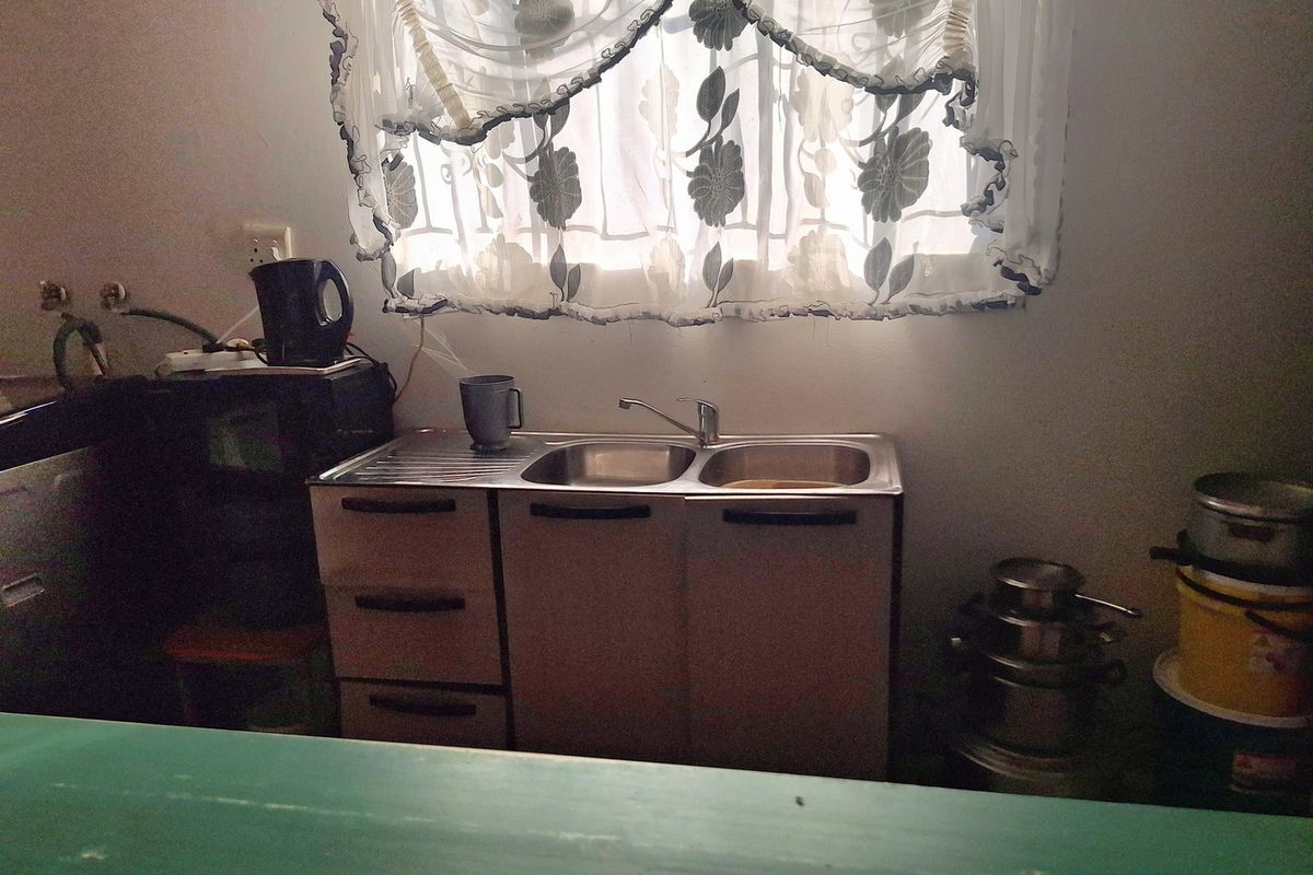 A compact kitchen area featuring a stainless steel double sink unit with built-in cabinetry and a window with decorative curtains.