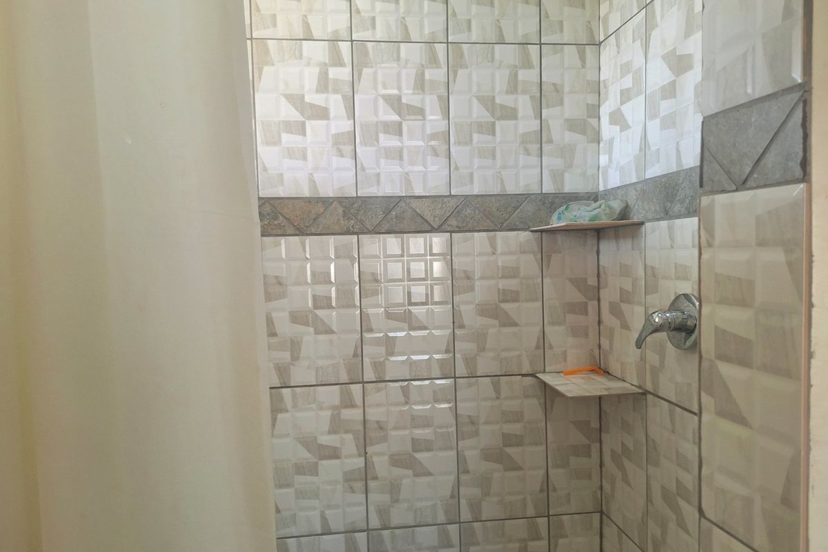 A tiled shower enclosure featuring built-in corner shelving and a chrome shower mixer tap.